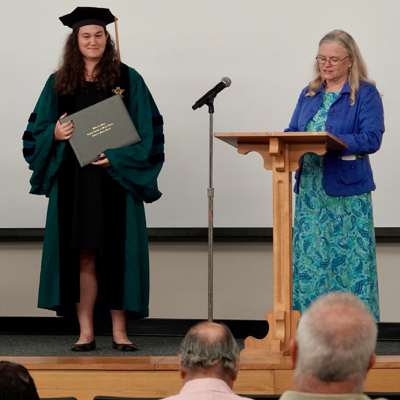 Dr. Linda Schaffner (R), Associate Dean of Academic Studies, takes a moment during commencement to extol the many accomplishments of Dr. Sarah Pease (L). 