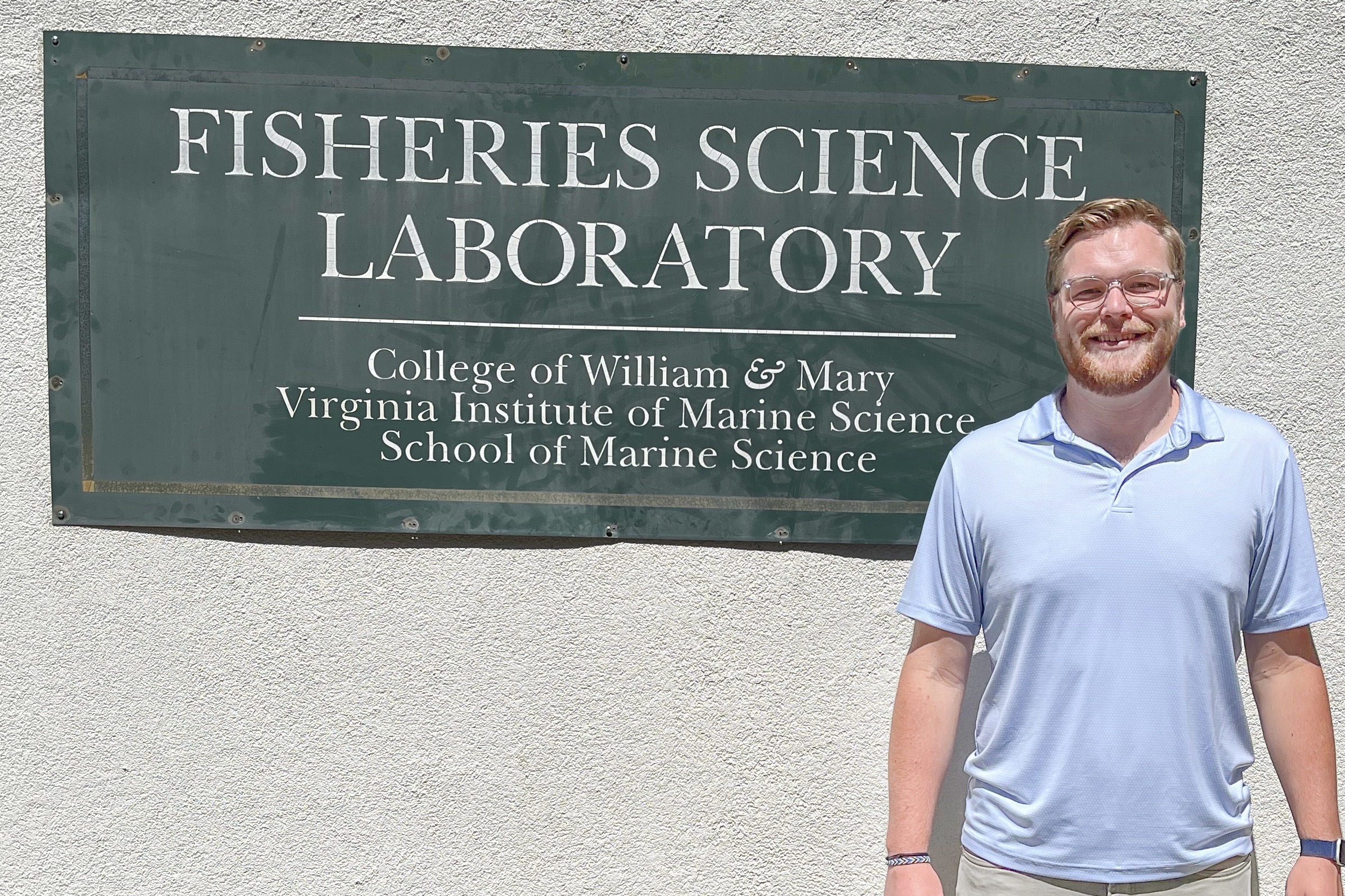 M.A. student Will standing in front of a building sign that says 'Fisheries Science Laboratory'
