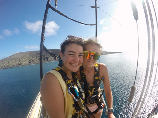 Incoming MS student Catherine Czajka (L) and classmate Olivia DeWitt aloft aboard the SSV Robert C. Seamans with SEA Semester in October 2019. NASA researchers joined their cruise to explore the landform behind them, Hunga Tonga-Hunga Ha'apai, a newly-formed volcanic island in the Kingdom of Tonga which could provide insight into the formation of craters on Mars. © Frank Wenninger.
