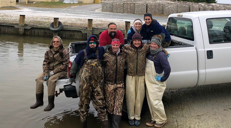 A team of ABC scientists in field gear posed on the bed of a work truck, getting ready to sample the long line system on the Choptank River