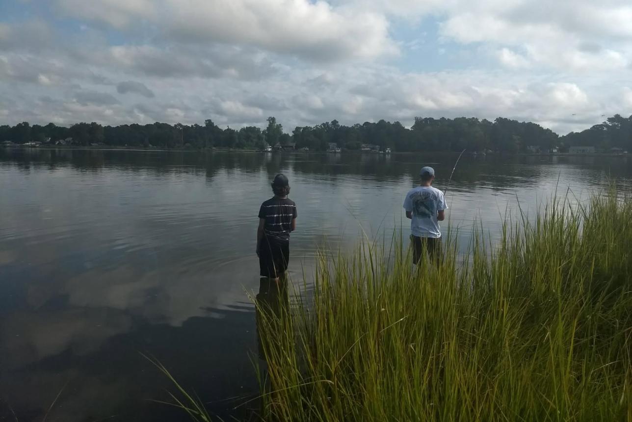 Two young men standing knee deep in coastal waters fishing